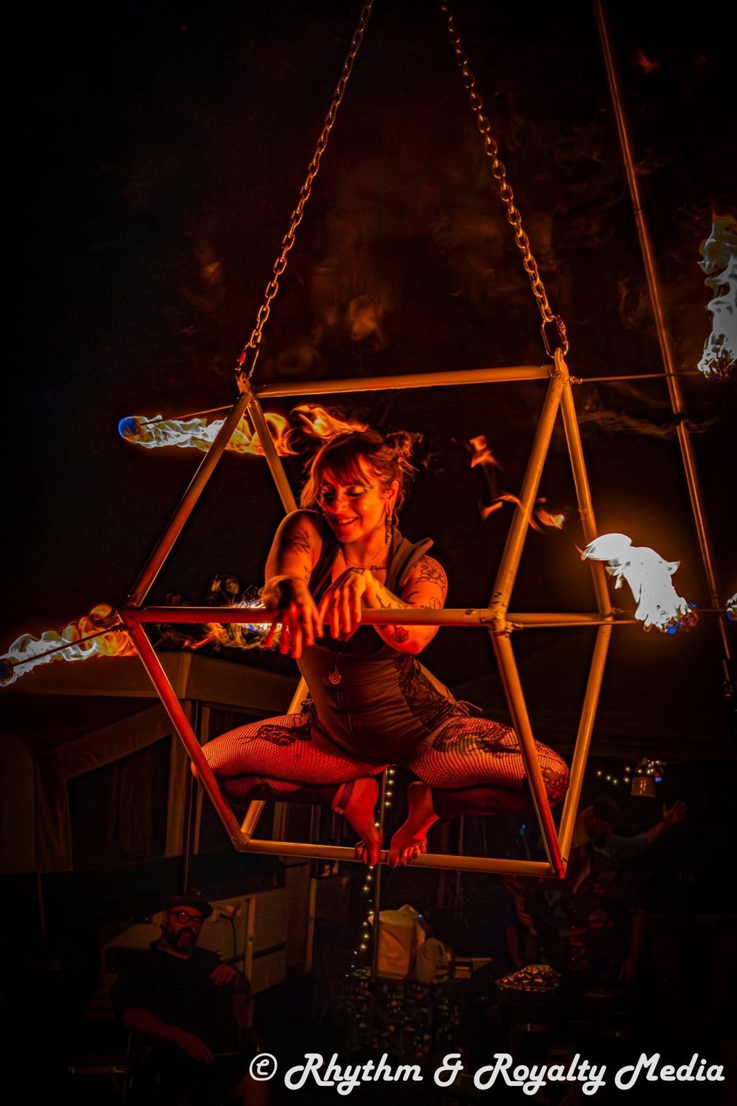 Performer in a hanging cube lit by fire
